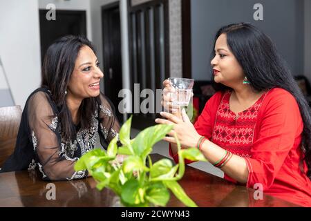 Ritratto di due amici femminili seduti a casa e che hanno una conversazione amichevole, sorridendo le donne, tenendo un bicchiere d'acqua e chiacchierando. Foto Stock