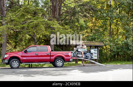 Shenandoah Valley, VA, USA 09/27/2020: Un anziano motorista sta scaricando la sua moto dal tronco di un pick-up rosso Ford F150 XTR facendo lentamente marcia su u Foto Stock