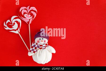 Pupazzo di neve che tiene tradizionali caramelle di Natale a forma di cuore su sfondo rosso. Informazioni sul biglietto di auguri Foto Stock