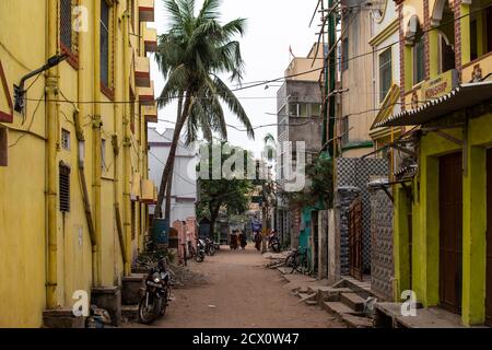 Puri, India - 3 febbraio 2020: Alcune persone non identificate camminano su una piccola strada sterrata locale con un edificio giallo e moto parcheggiate Foto Stock