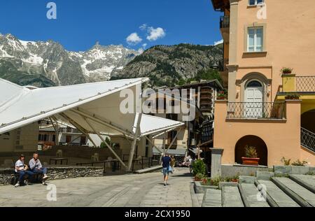 Vista sulla strada del centro della famosa città montana con lo spazio eventi Jardin de l'Ange e il massiccio del Monte Bianco in estate, Courmayeur, Aosta Italia, Foto Stock