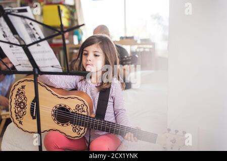 6 anni ragazza pratica chitarra lezione con papà in lo sfondo Foto Stock