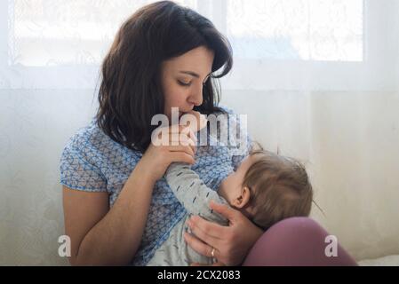 Madre amabile che bacia la mano del bambino mentre allatta Foto Stock