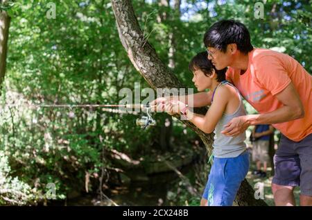 Un padre si allunga per aiutare a tenere la pesca del figlio asta ferma Foto Stock
