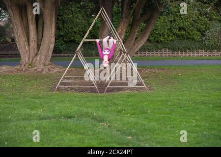 Ragazza giovane appesa capovolta su attrezzature per il parco giochi presso il parcheggio Foto Stock