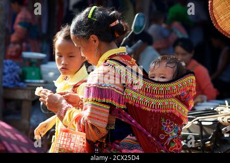 Fiore Hmong donna con bambino nel portatore del bambino. COC Ly, Vietnam Foto Stock