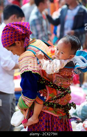 Donna Hmong con bambino in baby carrier sulla schiena, Can Cau mercato, vicino Bac ha, Lao Cai Provincia, Vietnam Foto Stock