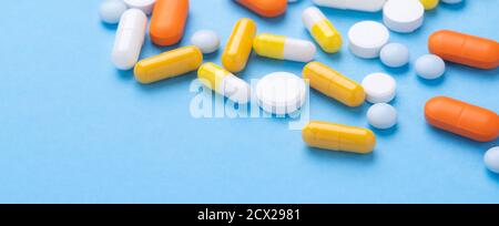 Compresse multicolori e pillole capsule su sfondo blu Tucciole di varie compresse e pillole di medicina assortite. Banner orizzontale - immagine Foto Stock