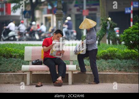 Venditore di giornali e man Reading, accanto al lago Hoan Kiem, Hanoi, Vietnam Foto Stock