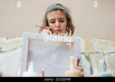 ragazza bianca mordendo un pennello mentre pensando come continuare la sua immagine. Foto orizzontale Foto Stock