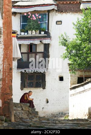 Monaco tibetano seduto su un gradino. Un'ispezione accurata rivela che sta utilizzando un telefono cellulare. Monastero di Tashilunpo, Shigatse, Tibet Foto Stock