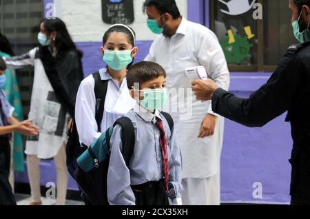 L'amministrazione scolastica ufficiale delle istituzioni educative primarie controlla la temperatura corporea degli studenti all'ingresso della scuola come misura preventiva contro la diffusione del coronavirus (COVID-19), dopo la riapertura della scuola quasi sei mesi di chiusura a causa della pandemia di Covid-19, a Peshawar mercoledì 30 settembre 2020. Foto Stock