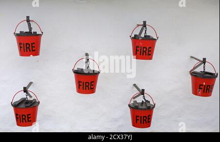 Sei vecchie benne Red Fire con coperchi neri appesi Un muro bianco a Gibilterra Foto Stock