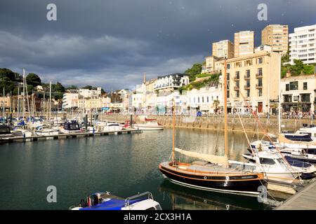 Porto di Torquay illuminato dal sole con nuvole minacciose che incombono in alto. Molte barche da pesca sono ormeggiate nel porticciolo Foto Stock