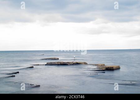 Lunga esposizione di rocce che si stagliano dall'acqua e dal cielo adramatico, onde calme e formazioni rocciose affilate, splendida vista sull'oceano e sul cielo a Kimmeridge Foto Stock