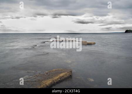 Lunga esposizione di rocce che si stagliano dall'acqua e dal cielo adramatico, onde calme e formazioni rocciose affilate, splendida vista sull'oceano e sul cielo a Kimmeridge Foto Stock