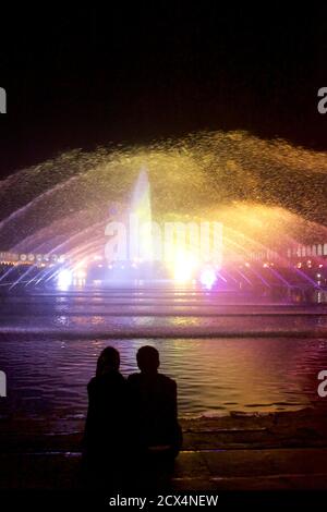 La coppia trainiana si stagliava contro le luci e la fontana di Piazza Imam di notte. Isfahan, Iran Foto Stock