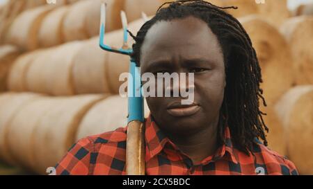 Ritratto di un giovane agricoltore africano con forchetta sopra la spalla di fronte al fienato. Foto di alta qualità Foto Stock