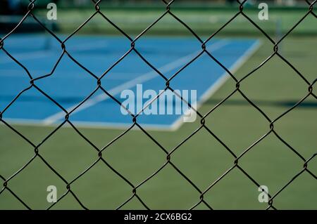particolare di una vista su un campo da tennis sintetico blu attraverso una recinzione Foto Stock