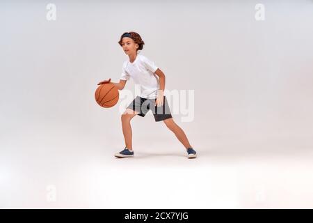 Miglior sport per i bambini. Scatto a tutta lunghezza di un ragazzo adolescente che gioca a basket mentre si trova isolato su sfondo grigio, scatto in studio Foto Stock