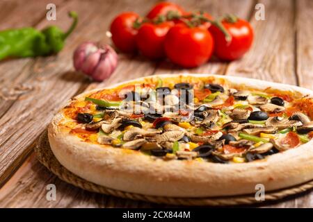 primo piano di pizza con verdure e pepperoni su fondo ligneo Foto Stock