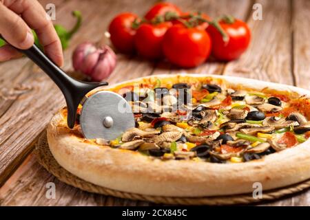 primo piano di tagliando a mano la pizza con verdure e pepperoni sfondo di legno Foto Stock