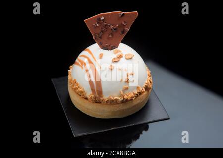 Torta individuale con glassa a specchio e cioccolato croccante, su fondo nero. Foto Stock