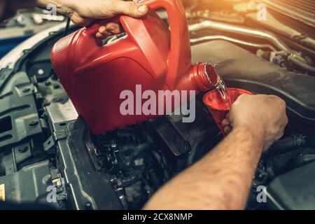 Le mani dell'operatore versano l'olio motore di lavaggio nel motore per rimuovere i depositi di carbonio durante la manutenzione automatica, correggere il cambio di fasatura nella vettura Foto Stock