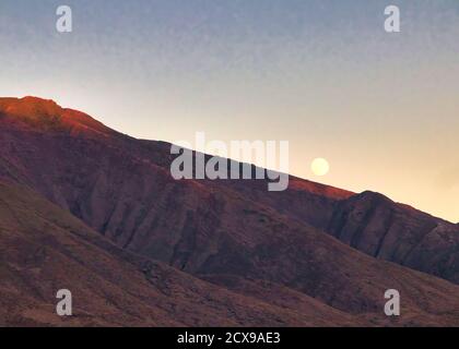 Luna piena che si erge su una cresta delle montagne di maui ad ovest al tramonto. Foto Stock