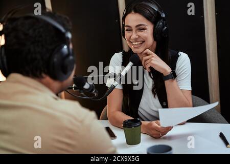 Portait di felice radio host femmina sorridente, ascoltando ospite maschile, presentatore e tenere un copione di moderare uno spettacolo dal vivo in studio Foto Stock