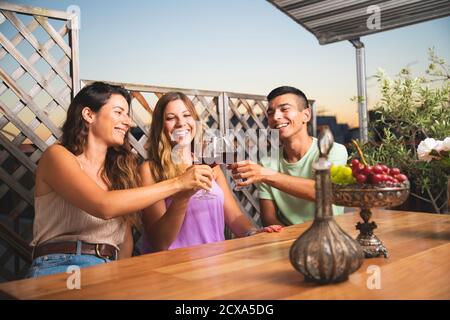 Tre amici che si acclamano e si acclamano con bicchieri di vino al balcone. Persone sedute al balcone Foto Stock