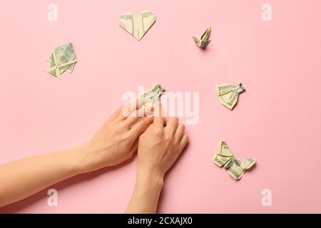 Donna che fa figure di origami dalle banconote del dollaro su sfondo di colore Foto Stock