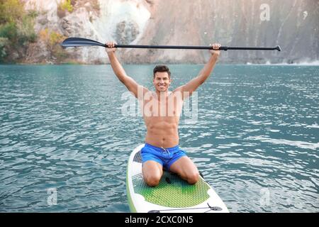 Giovane uomo che usa il paddle board per surfing sup in fiume Foto Stock