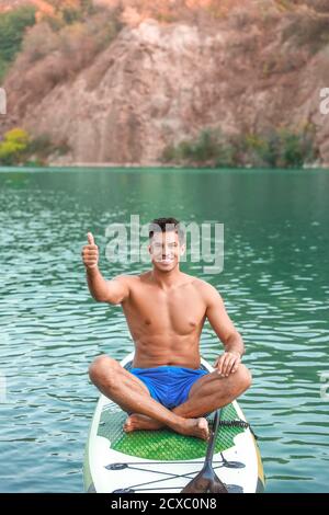 Giovane uomo che usa il paddle board per surfing sup in fiume Foto Stock