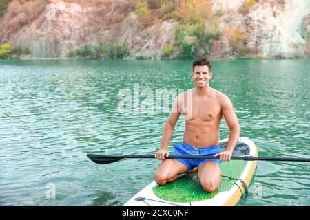 Giovane uomo che usa il paddle board per surfing sup in fiume Foto Stock