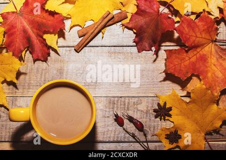 Tazza di caffè con latte e foglie gialle su fondo di legno. Composizione accogliente per il design autunnale. Foto Stock