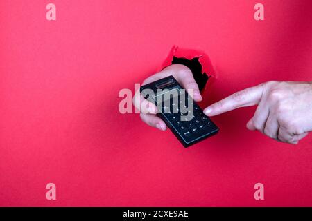 Calcolatore nero in mano e tasti premuti con le dita. Sfondo di carta rosso Foto Stock