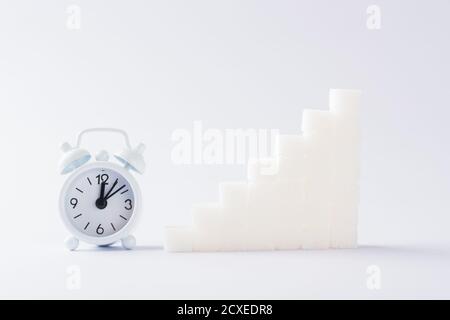 Pila ascendente di cubi di zucchero grafico e sveglia, studio girato isolato su sfondo bianco, salute elevato rischio di sangue di diabete concetto Foto Stock