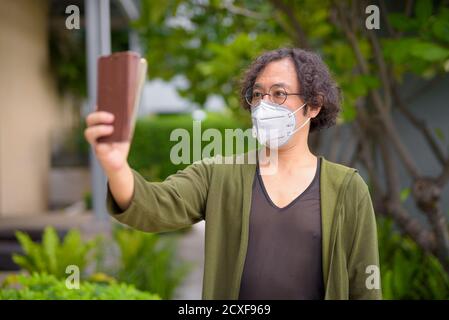 Uomo giapponese con maschera che prende selfie nel giardino sul tetto Foto Stock