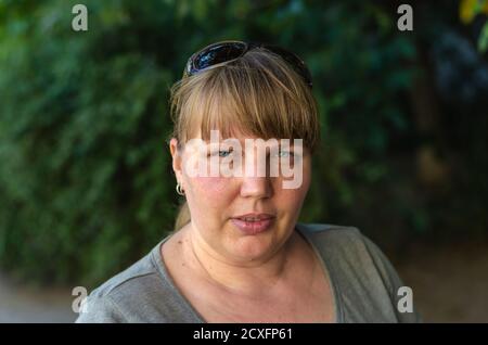 Ritratto di una donna adulta senza trucco e rossetto all'aperto. Donna con lunghi capelli biondi e occhiali da sole sulla testa. Età 40-45. beau femmina naturale Foto Stock