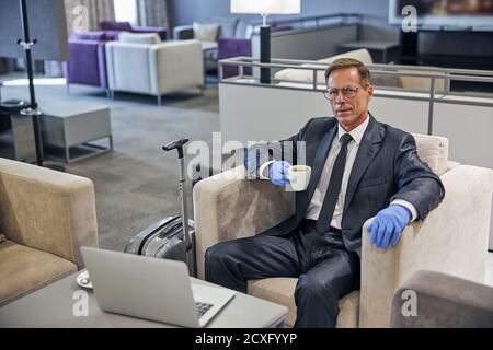 Uomo d'affari sorridente con una tazza di caffè e un computer portatile prima del volo Foto Stock