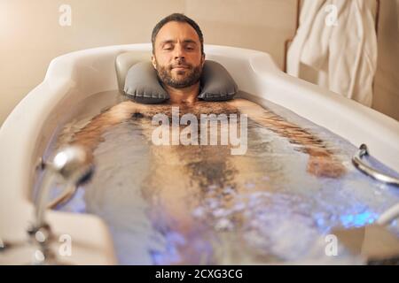 Bel giovane uomo che prende il bagno nel salone termale Foto Stock