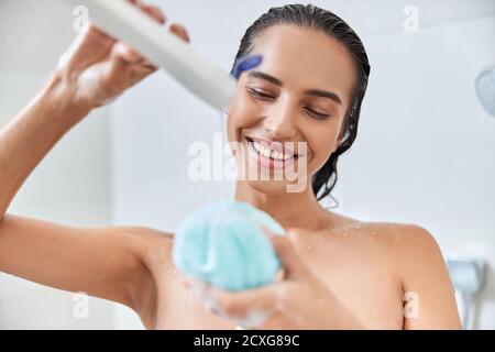 Giovane donna di charme che versa gel doccia sulla loofah bagno Foto Stock