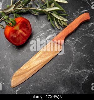 coltello in legno con pomodoro su marmo nero in cucina Foto Stock