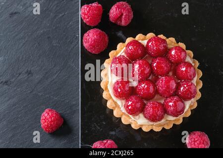 Tartlet con crema pasticcera e lamponi smaltati freschi, serviti su tavola di marmo nero su superficie in ardesia di pietra. Vista dall'alto Foto Stock