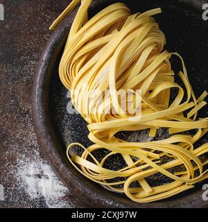 Tagliatelle di pasta italiana crude, non cotte in casa, con farina in vecchio vassoio di argilla su sfondo di legno scuro. Vista dall'alto con spazio per il testo. Immagine quadrata Foto Stock