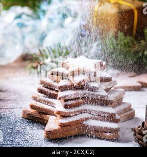 Stack di shortbread natalizi fatti in casa a forma di stella biscotti zucchero diverso taglia con polvere di zucchero spruzzato su vecchia superficie di legno con Decorazioni natalizie Foto Stock