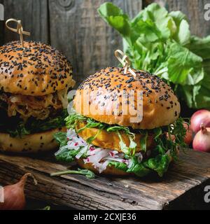 Due hamburger di verdure fatti in casa con patate dolci, rafano fresco e germogli di piselli, serviti su trivella di legno su sfondo di legno. Stile rustico scuro Foto Stock