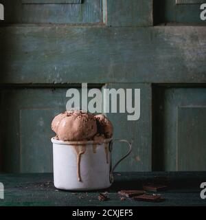 Tazza di alluminio vintage surgelata con palle di gelato al cioccolato fondente, servita con cioccolato fondente tritato su vecchio tavolo di legno. Stile rustico scuro. Spazio f Foto Stock