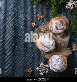 Croccini moderni per pasticceria, come croissant e muffin con zucchero in polvere, serviti con decorazioni natalizie e abeti su fondo di tessitura scura. In alto Foto Stock